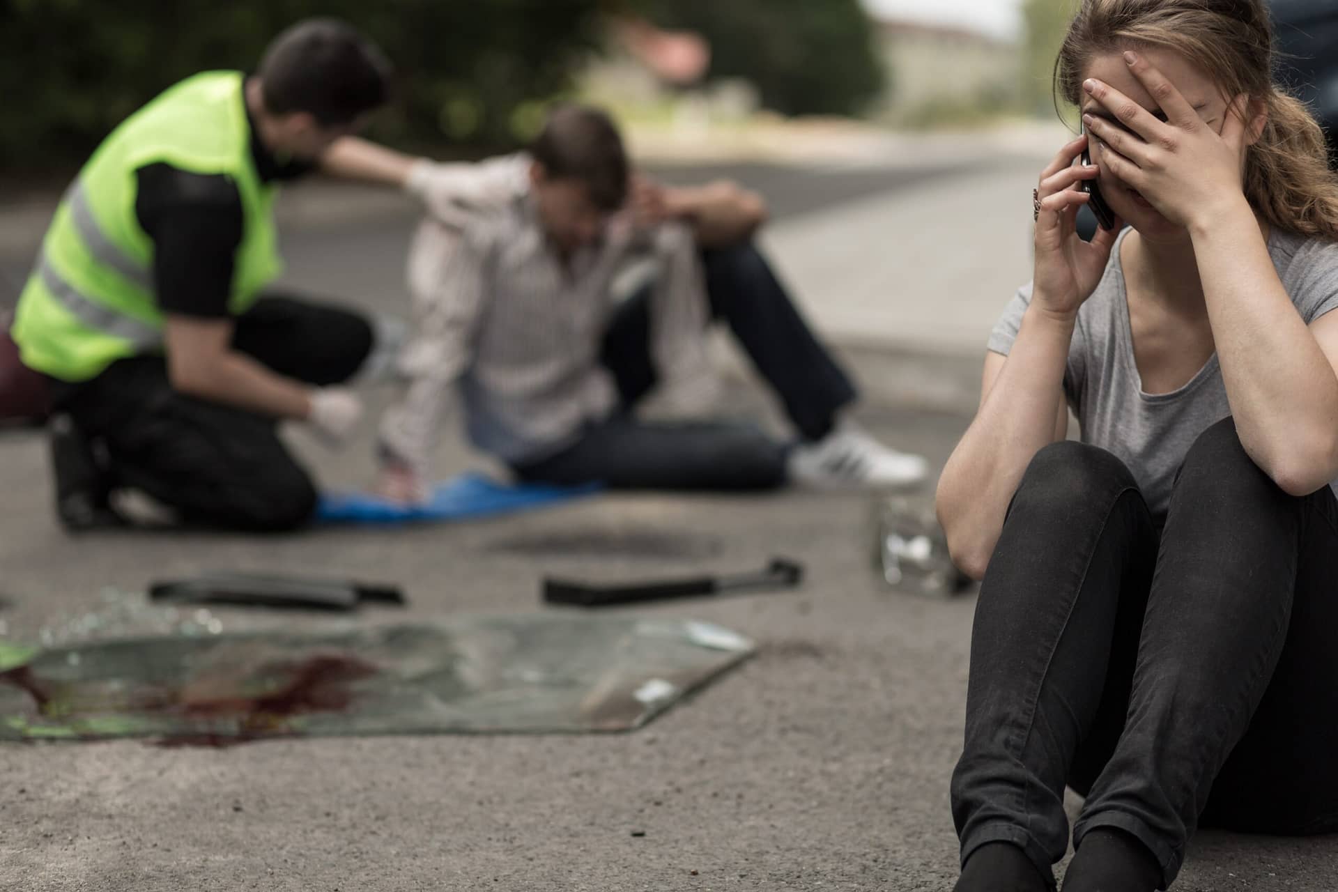 A distressed woman sits on the floor whilst an injured man with broken glass is behind her.