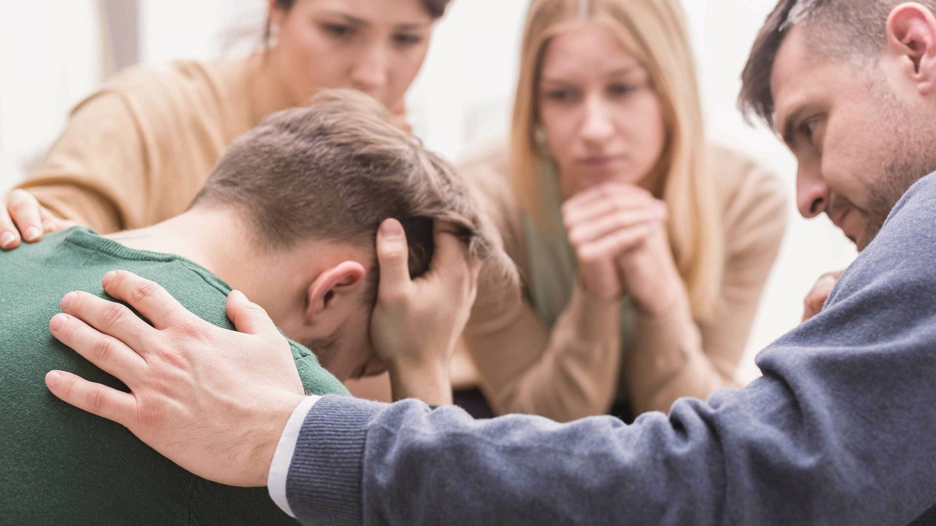 A group surrounds an upset man, offering heartfelt support.