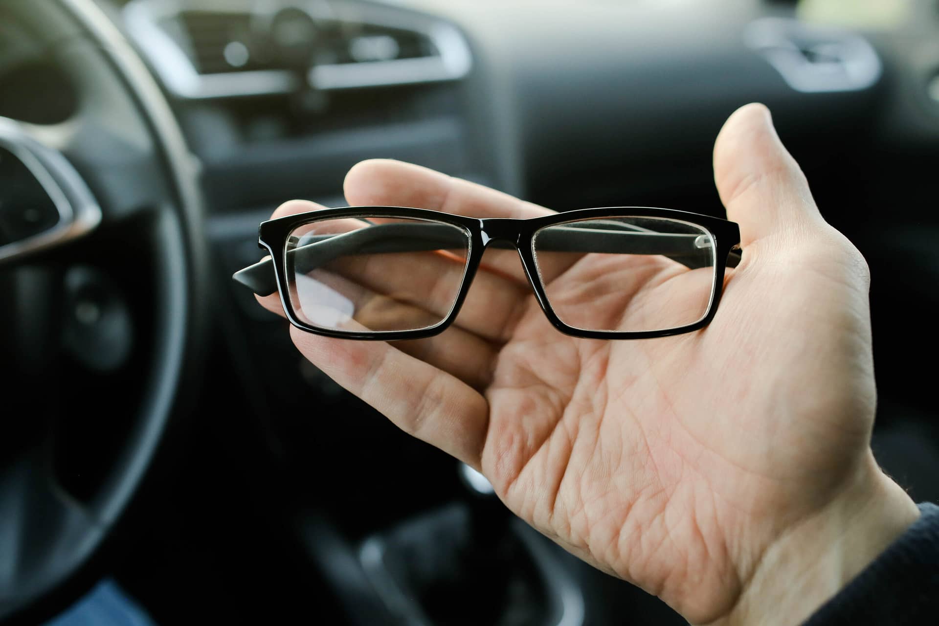 A person holds glasses sitting in a parked car.