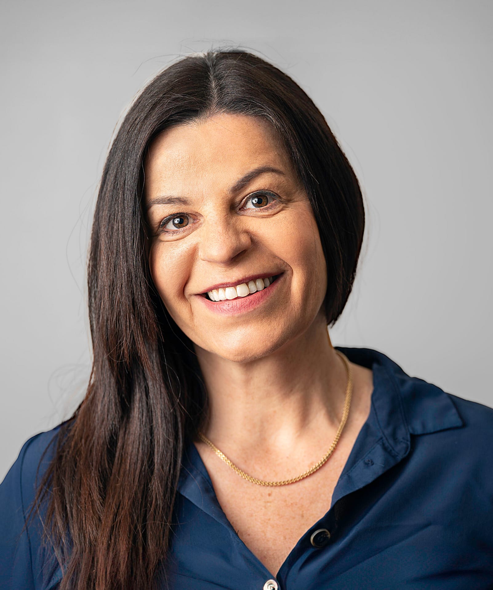 A woman in a blue shirt smiles in a bright setting.