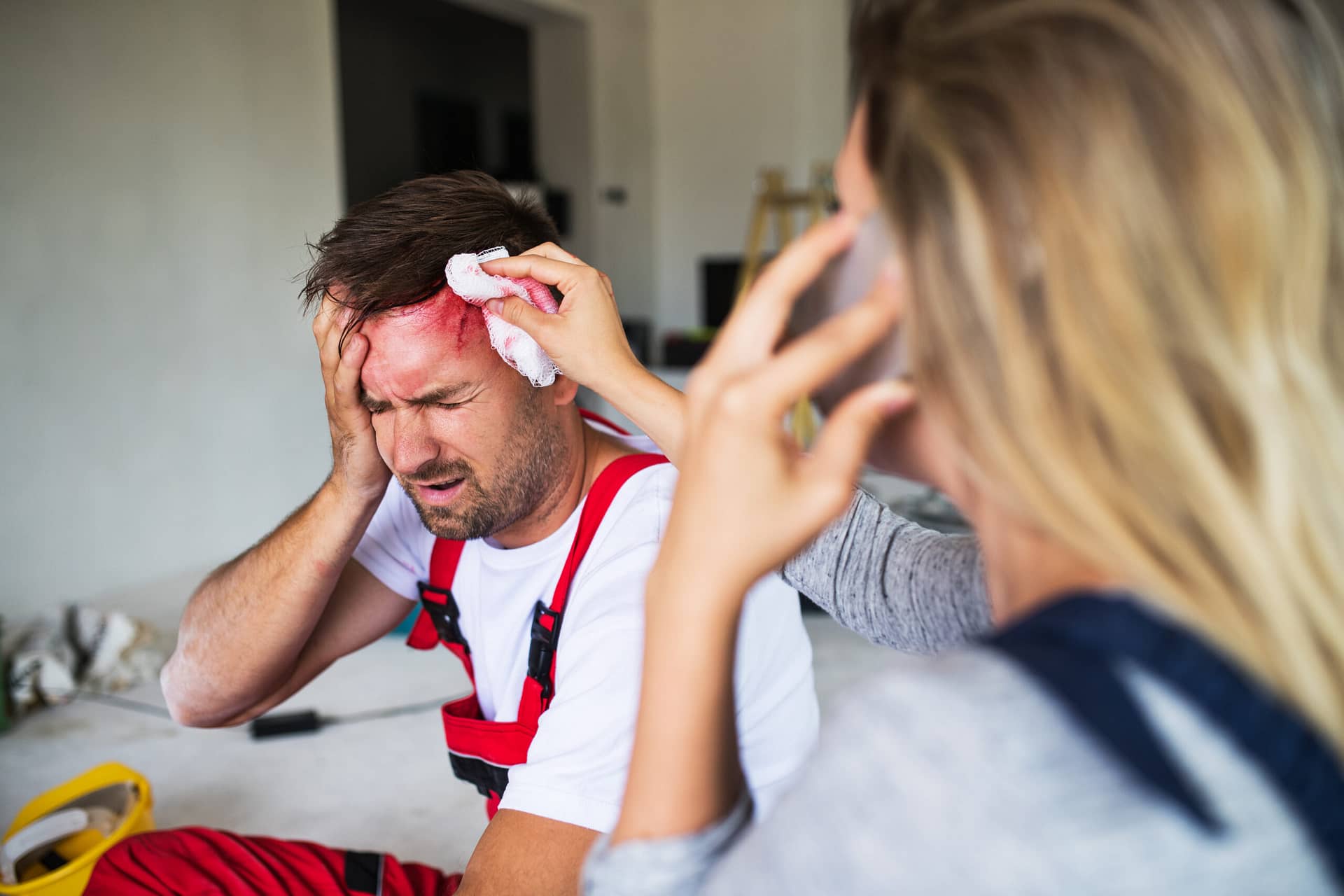 A woman is on the phone whilst attending to a man with a head wound.