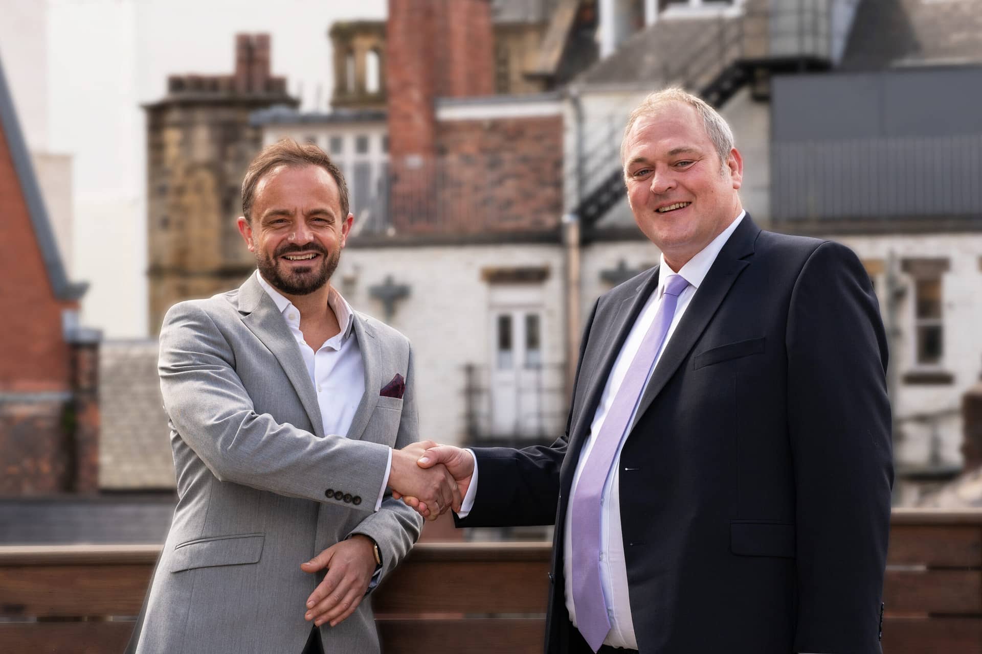 Two men shaking hands in front of a building, symbolising partnership.