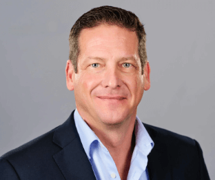 A man with short brown hair, wearing a shirt and suit jacket