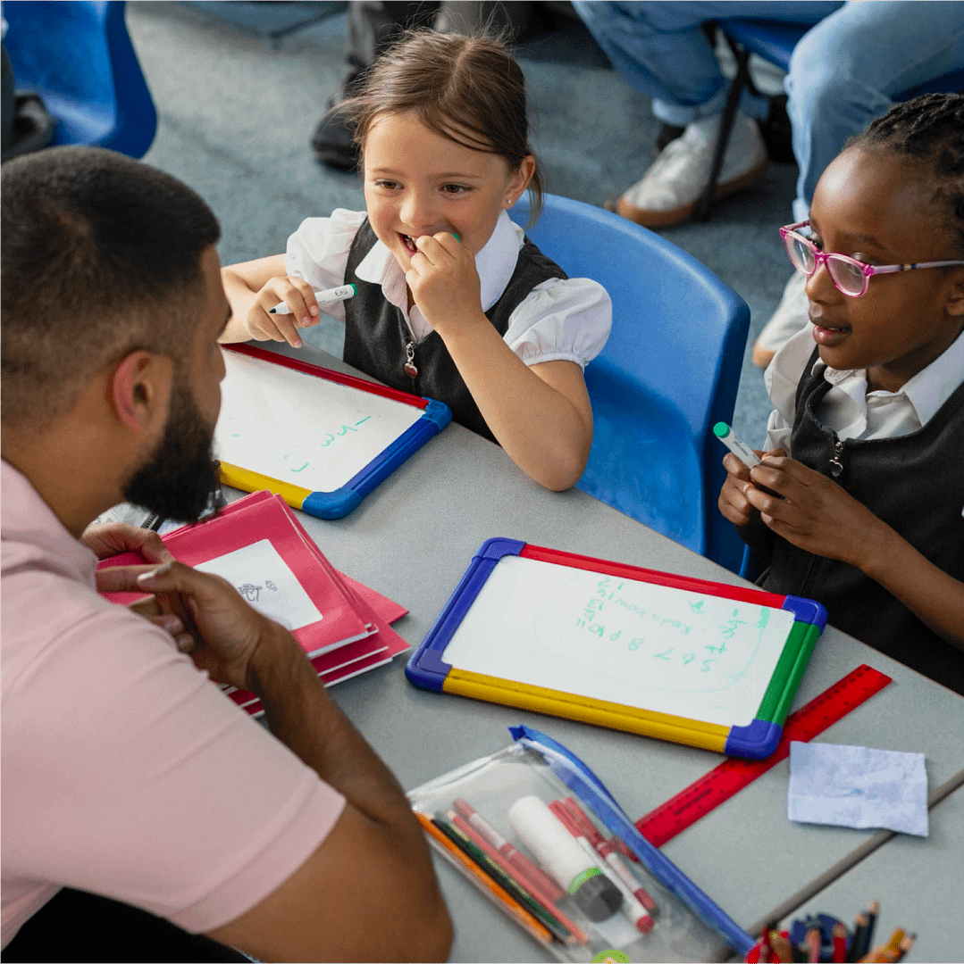 A teacher working with two primary school pupils using whiteboards in class.
