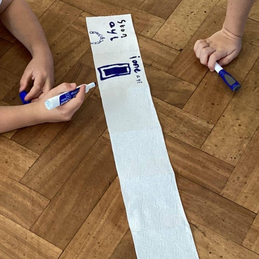 Pupils drawing symbols with blue markers on a long strip of paper.