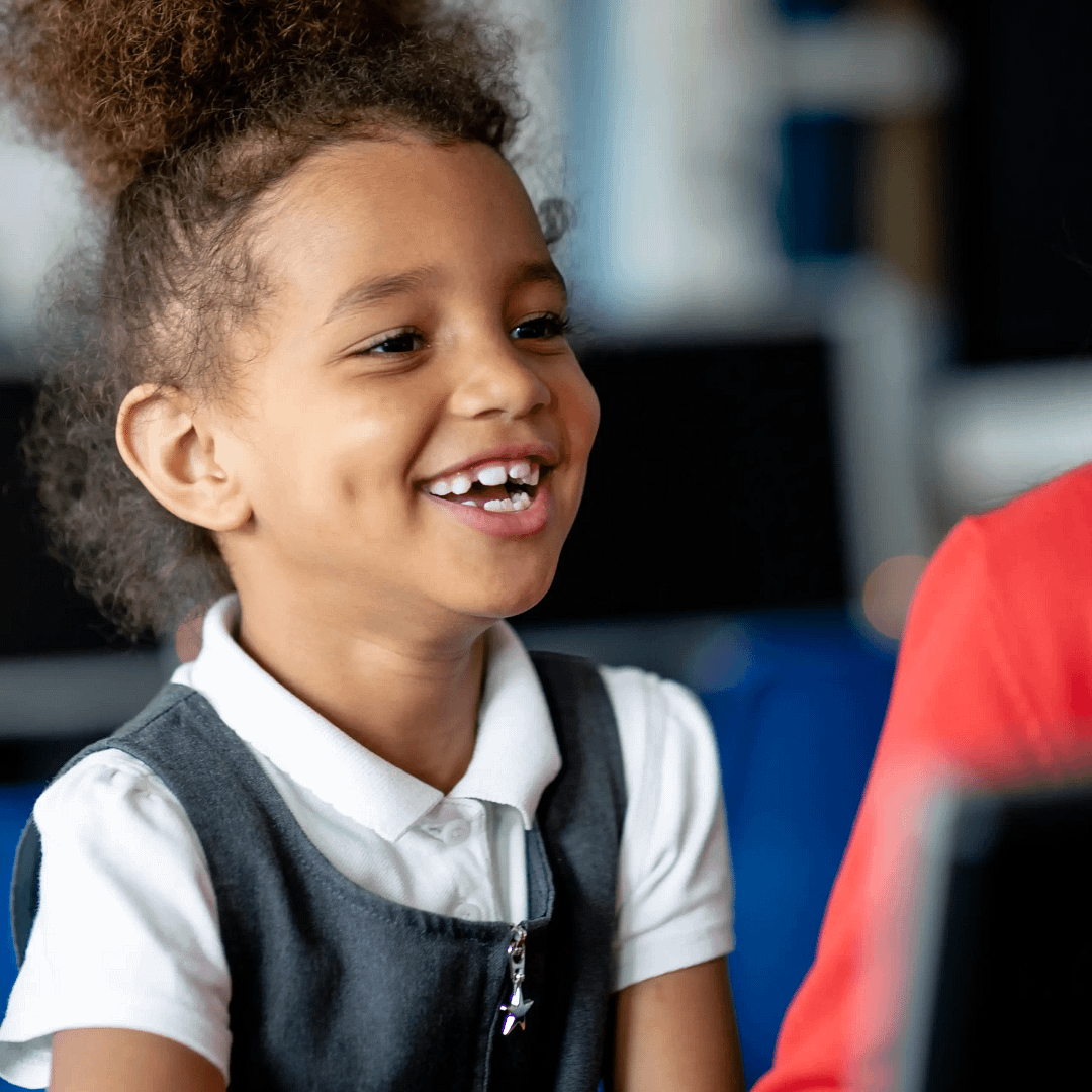 A happy girl wearing grey school uniform sits in a classroom.