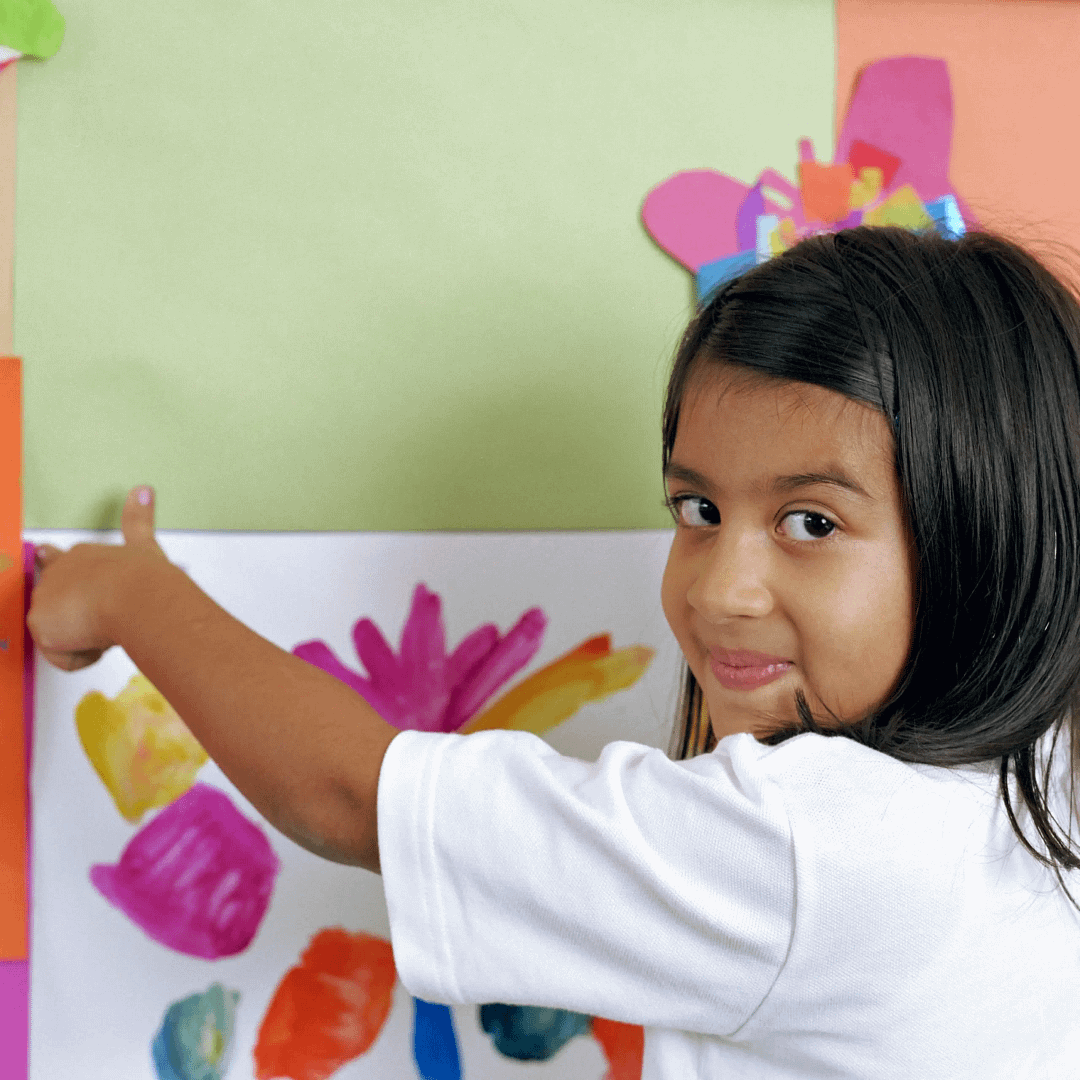 Smiling child points to their colourful painting displayed on a classroom wall.