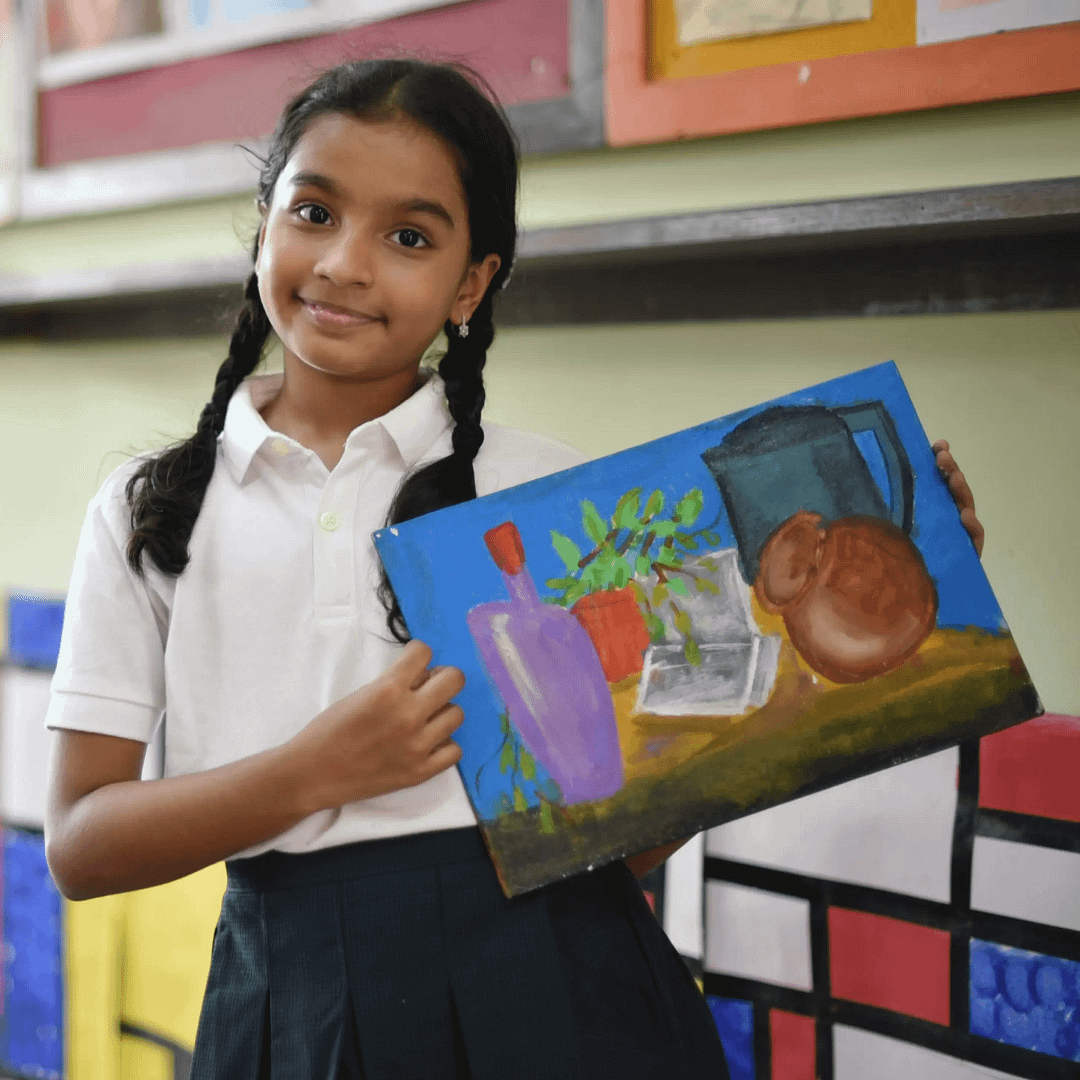 Girl in school uniform proudly holding her still life painting of bottles, a jug, a potted plant, and a pot on a table with a blue background.