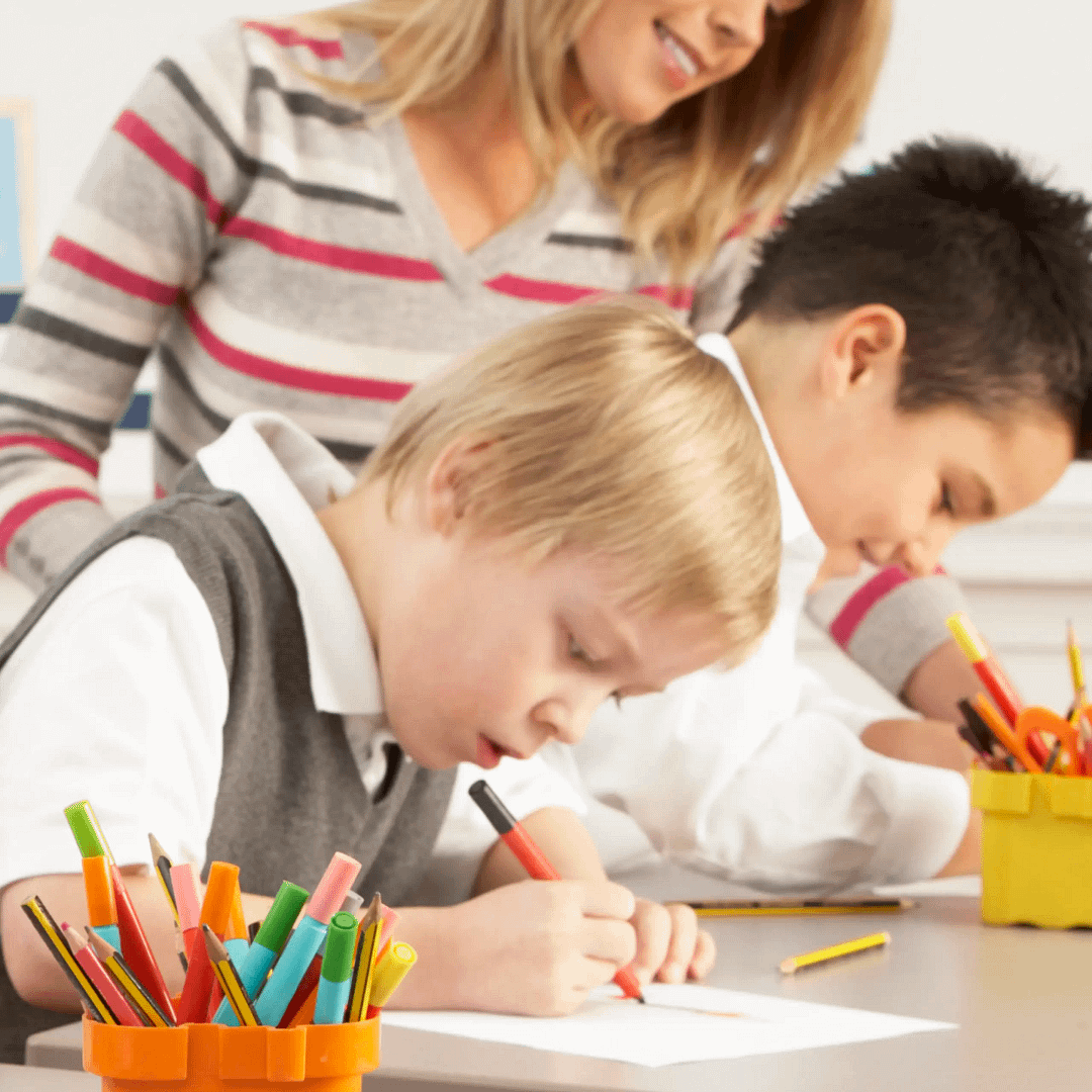 Boys drawing with pencils and markers as teacher looks on.