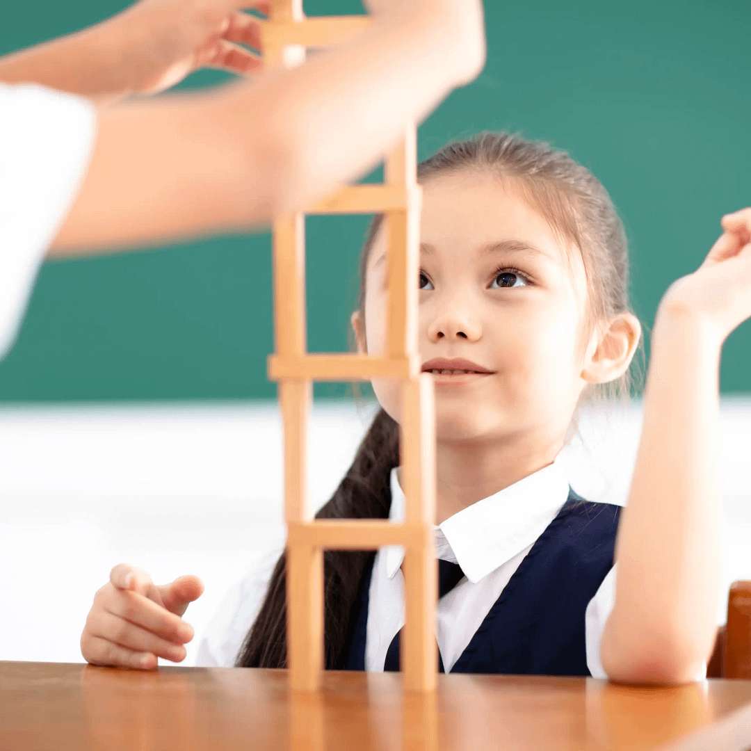 Girl in school uniform smiling while building a tall tower from wooden blocks.