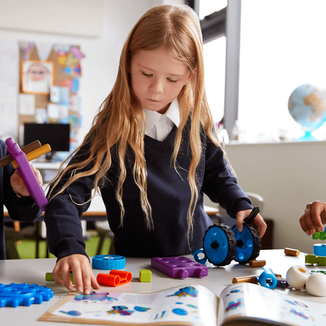 Child building with colourful plastic gears and wheels while following instructions in a book.