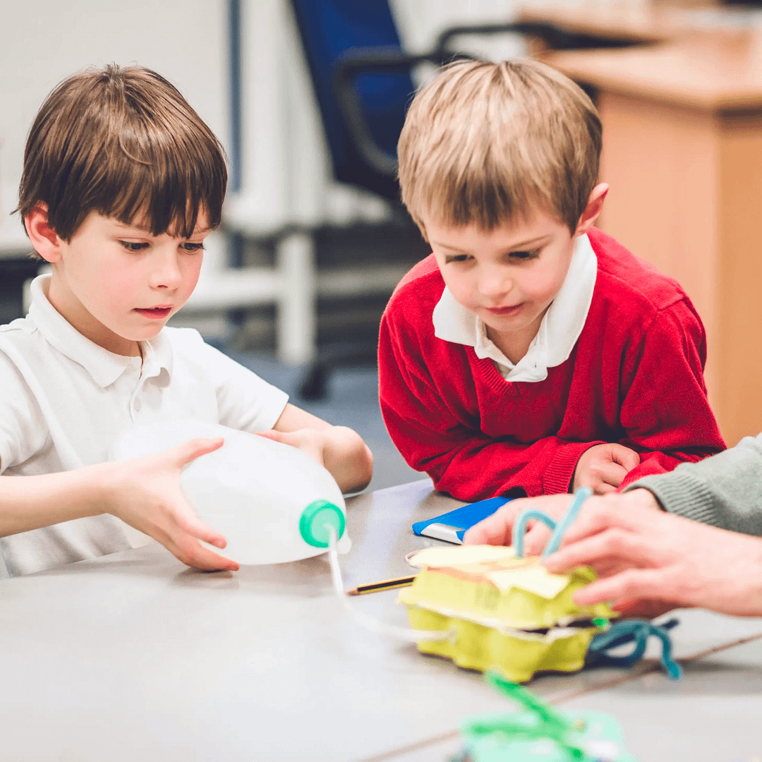 Two young boys working on a science project with recycled materials, including a plastic milk jug and egg cartons.