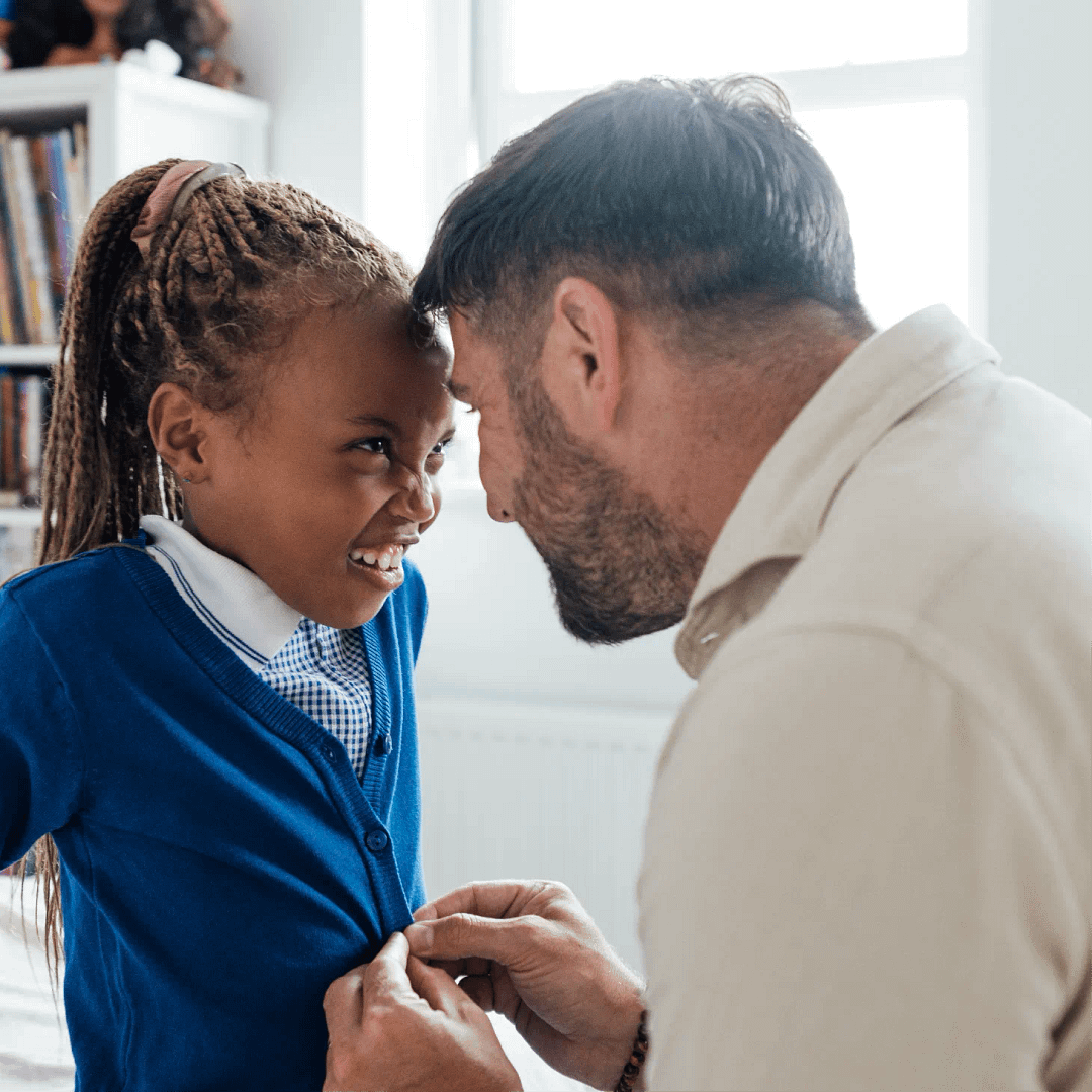 A parent helping their child button their school cardigan before school.