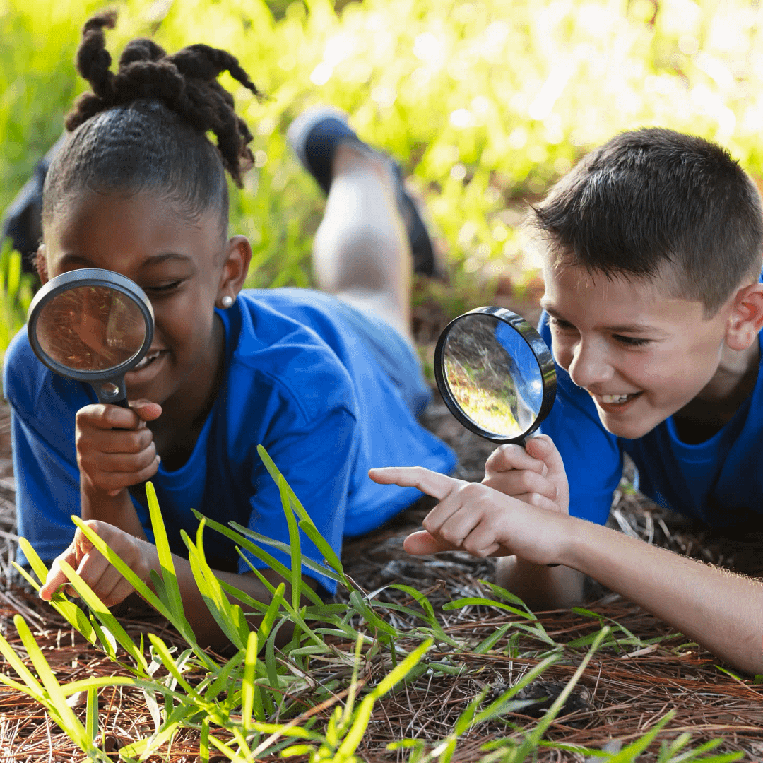 Two children using magnifying glasses to explore nature outdoors.
