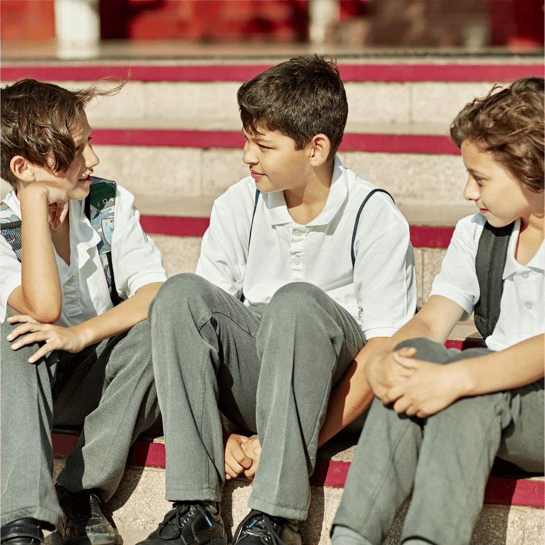 Three schoolboys in uniform sitting on outdoor steps talking together.