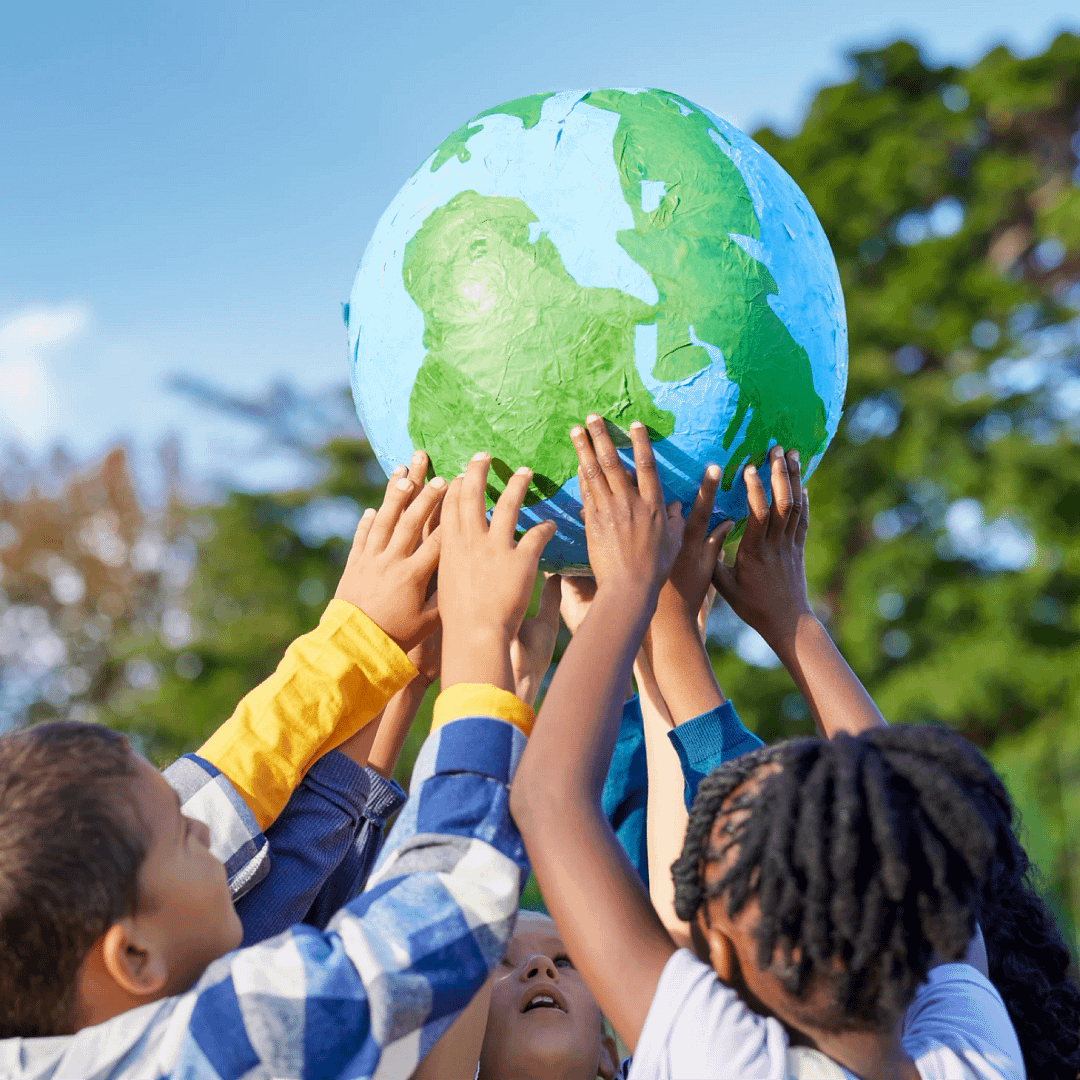 A group of children outdoors holding up a handmade globe together, showing teamwork and care for the planet.