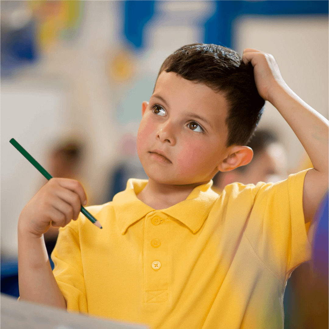 A child holding his hand to his head in thought, with a pencil in the other as he contemplates an answer.