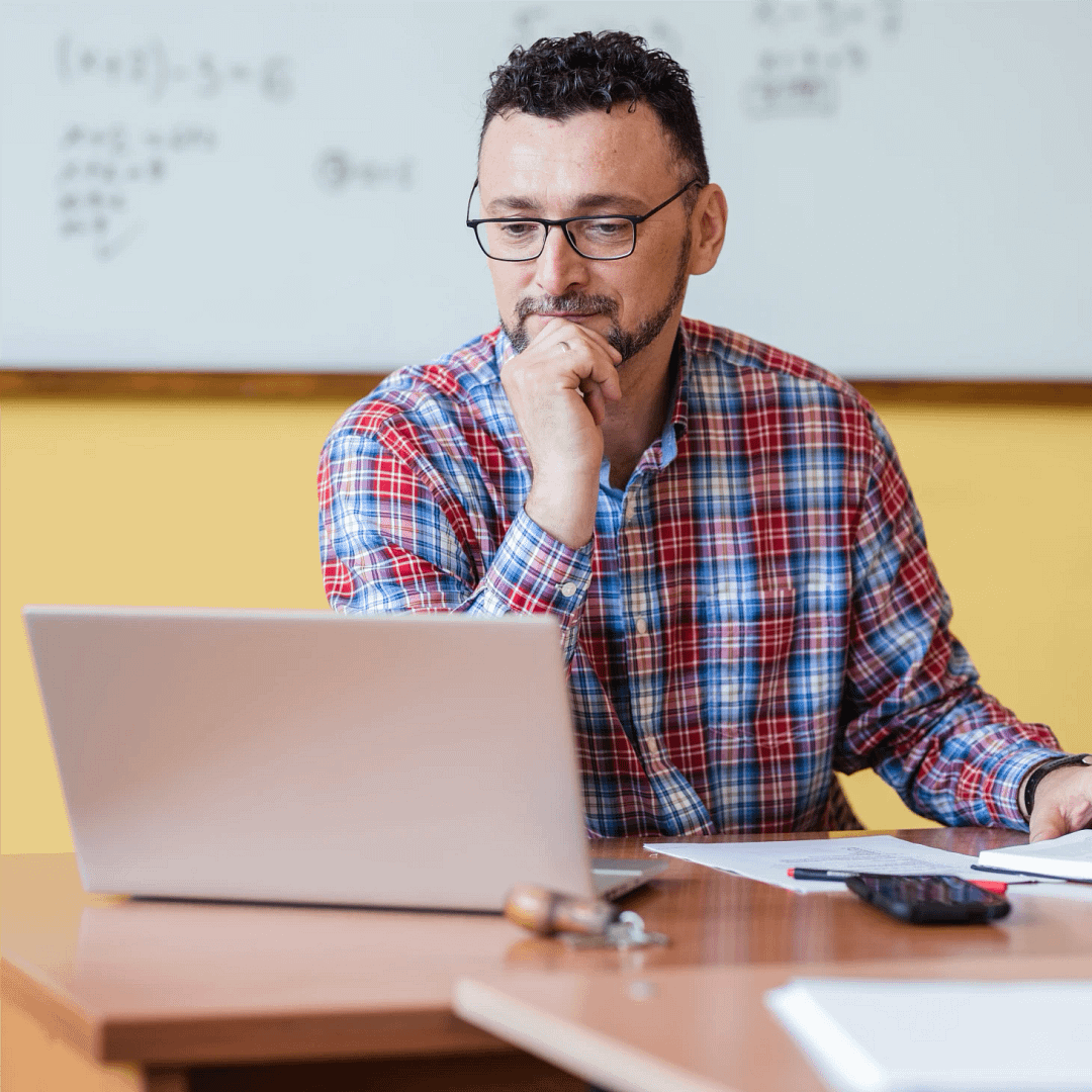 A teacher watching a webinar on his laptop in a classroom.