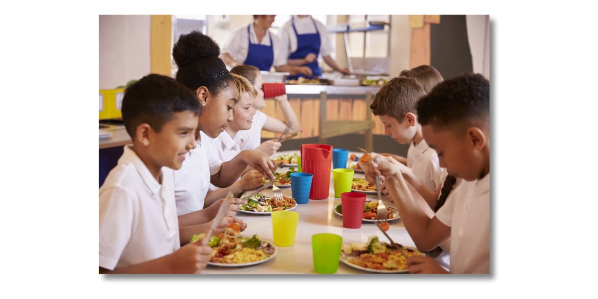 Primary children sat around a lunch table eating food