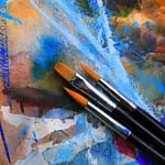 Three paintbrushes on top of a water colour image of different colours