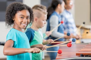 A girl smiling to the camera whilst she plays the xylophone