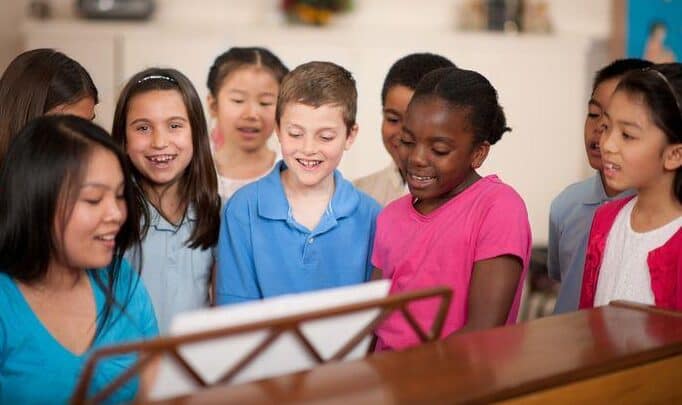 Children singing together around a piano.