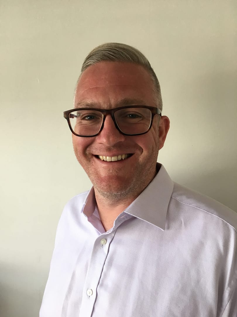 A white man smiles wearing a light shirt and glasses.