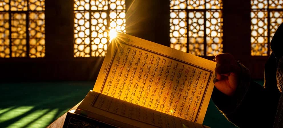 A Qur'an being read with light filtering through an Islamic screen.