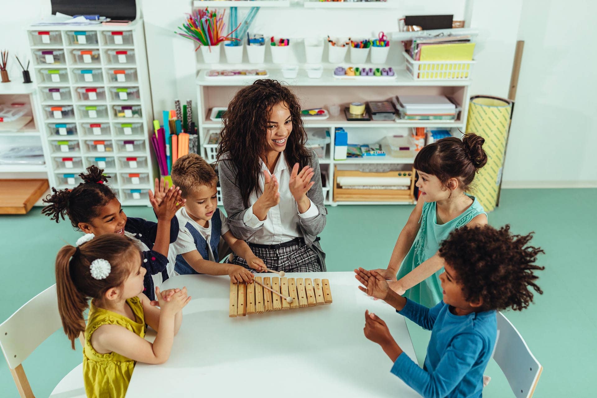 A teacher helping children play musical toys in a kindergarten classroom, fostering creative learning.