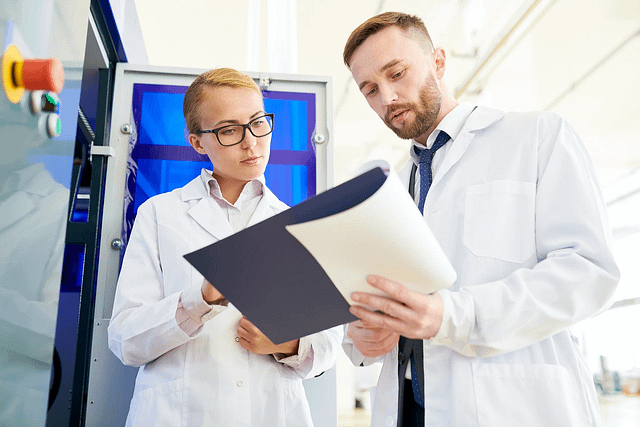 Male and female scientists at a refrigerated device consulting a document