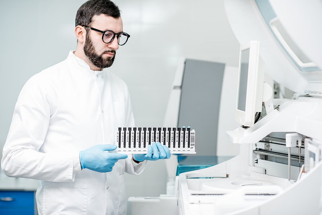 Male scientist entering a sample tube rack into an analyser