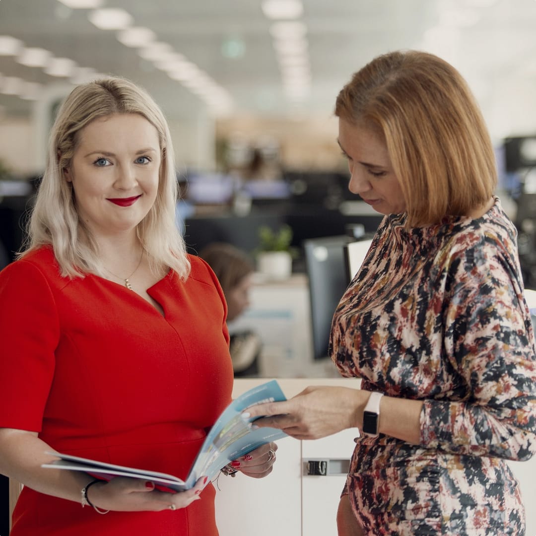 Two women in an office engage in conversation whilst reviewing a document.