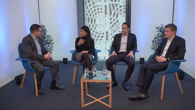 A group of four professionals engaged in discussion, seated around a table in a modern, well-lit office space.